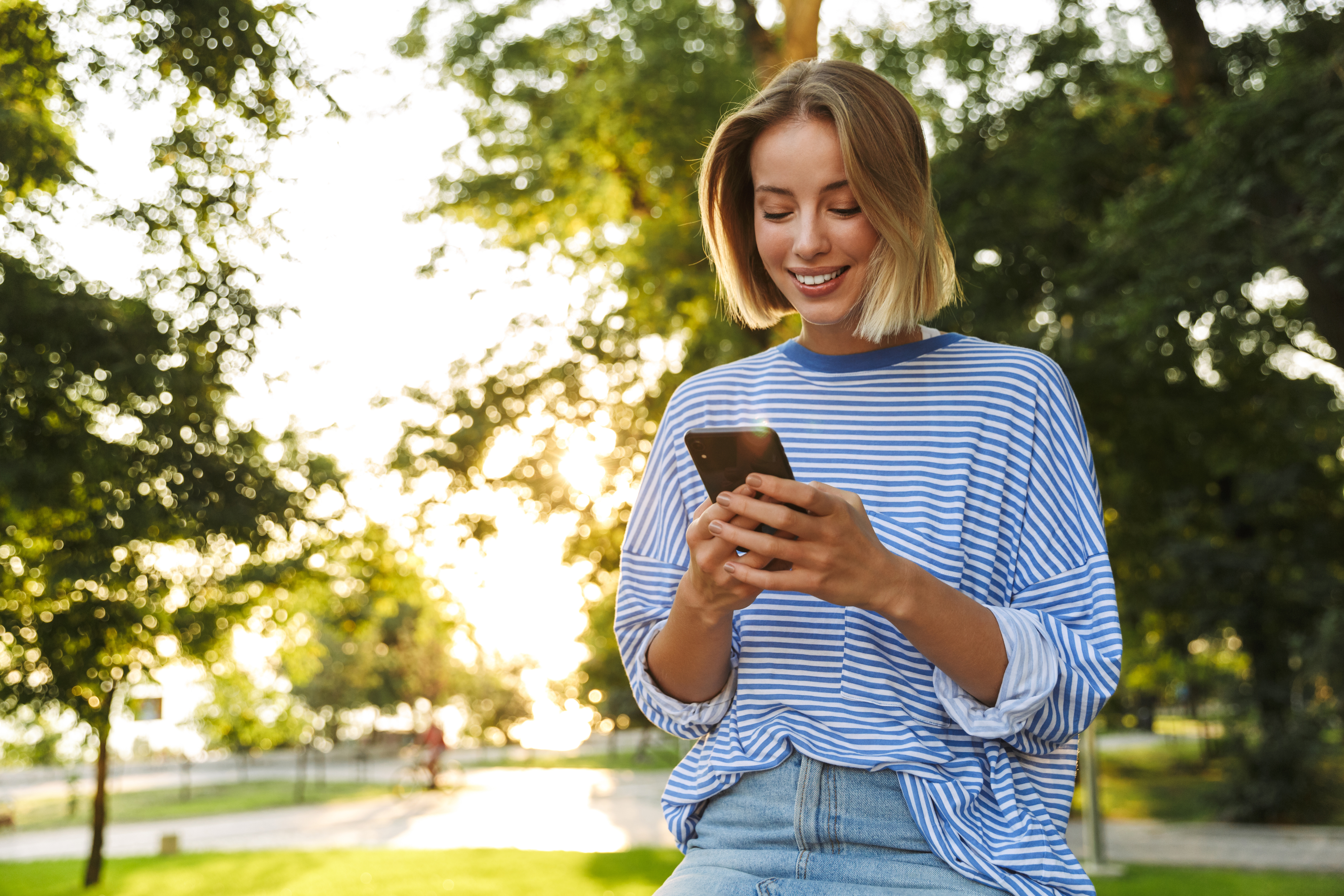 A woman sits in a park checking her credit union checking account balance on her smartphone.